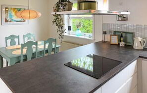 A kitchen with a black countertop, green chairs, a window with plants, and a hanging light fixture. - 3 bedroom stunning home in Tarm (Tarm)