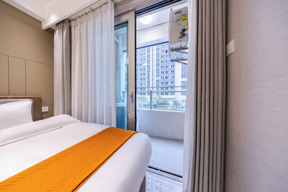 A hotel room with a bed, curtains, a window, and a view of a building.