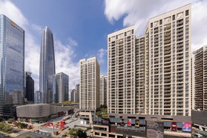 A modern urban skyline with high-rise buildings, a distinctive curved building, and a plaza with a large red sculpture. - BrisAudio-Visual X Ju (Shenzhen)