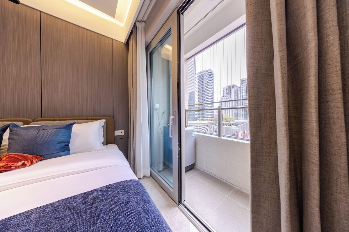 A modern hotel room with a large bed, a sliding glass door to a balcony, and a city view.