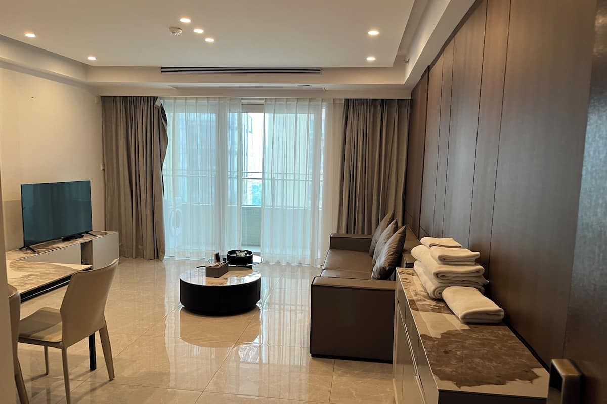 A modern living room with a flat-screen TV, a sofa, a coffee table, and a dining area with a chair and table.