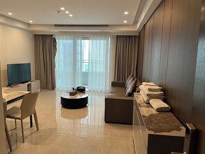 A modern living room with a flat-screen TV, a sofa, a coffee table, and a dining area with a chair and table. - BrisAudio-Visual X Ju (Shenzhen)