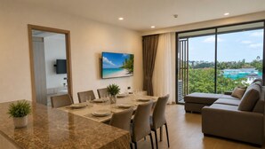 A modern living room with a dining area, a large window with a view, and a flat-screen TV mounted on the wall. - New 2 BR Apt Golf View - Ozone 108-156 (Thalang)