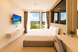 A modern hotel room with a large bed, a TV mounted on the wall, a desk with a chair, and large windows offering a view of the landscape. - New 2 BR Apt Golf View - Ozone 108-156 (Thalang)