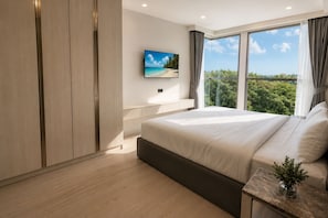 Une chambre moderne avec un grand lit, un téléviseur fixé au mur et une fenêtre donnant sur un paysage verdoyant.