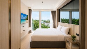 A modern bedroom with a large bed, a TV mounted on the wall, and a view of greenery outside. - New 2 BR Apt Golf View - Ozone 108-156 (Thalang)