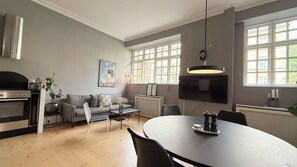 Une cuisine moderne dotée d’un four encastré, un coin repas avec une table ronde, un canapé et un téléviseur fixé au mur.