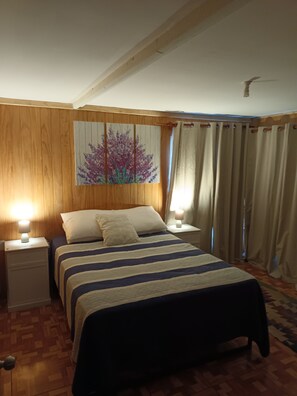 A bedroom with a bed, two bedside tables with lamps, a wooden headboard, a wall painting, and a window with curtains. - Whole lodge: cabin in Los Angeles, Chile 7 guests 3 bedrooms (los angeles)