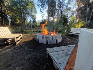 A campfire surrounded by wooden benches and a concrete fire pit in a forested area.