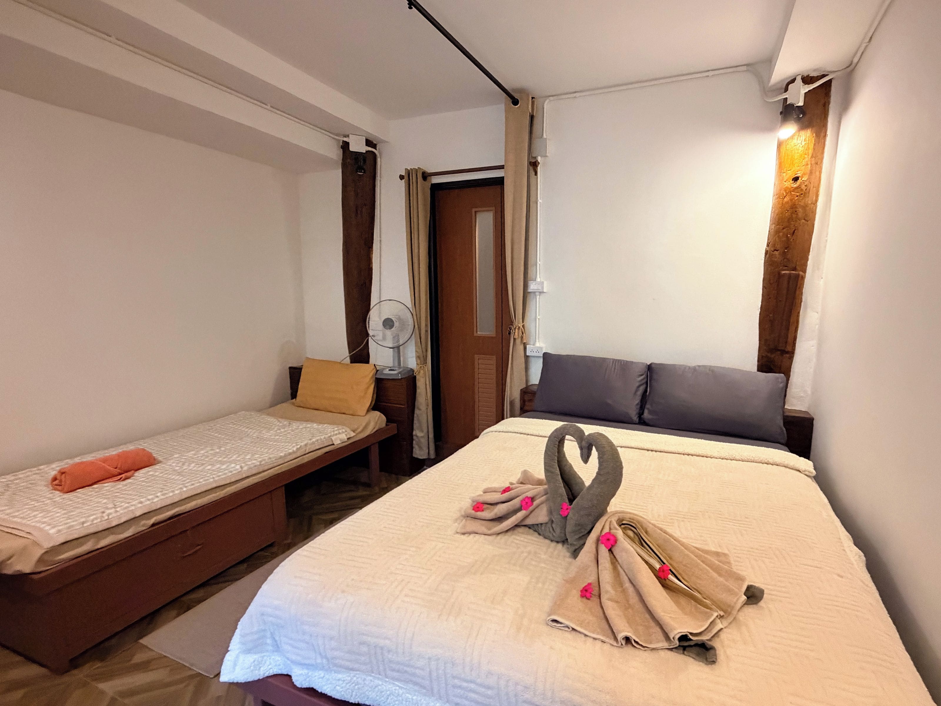 A room with a bed, a bedside table, a fan, and a door.