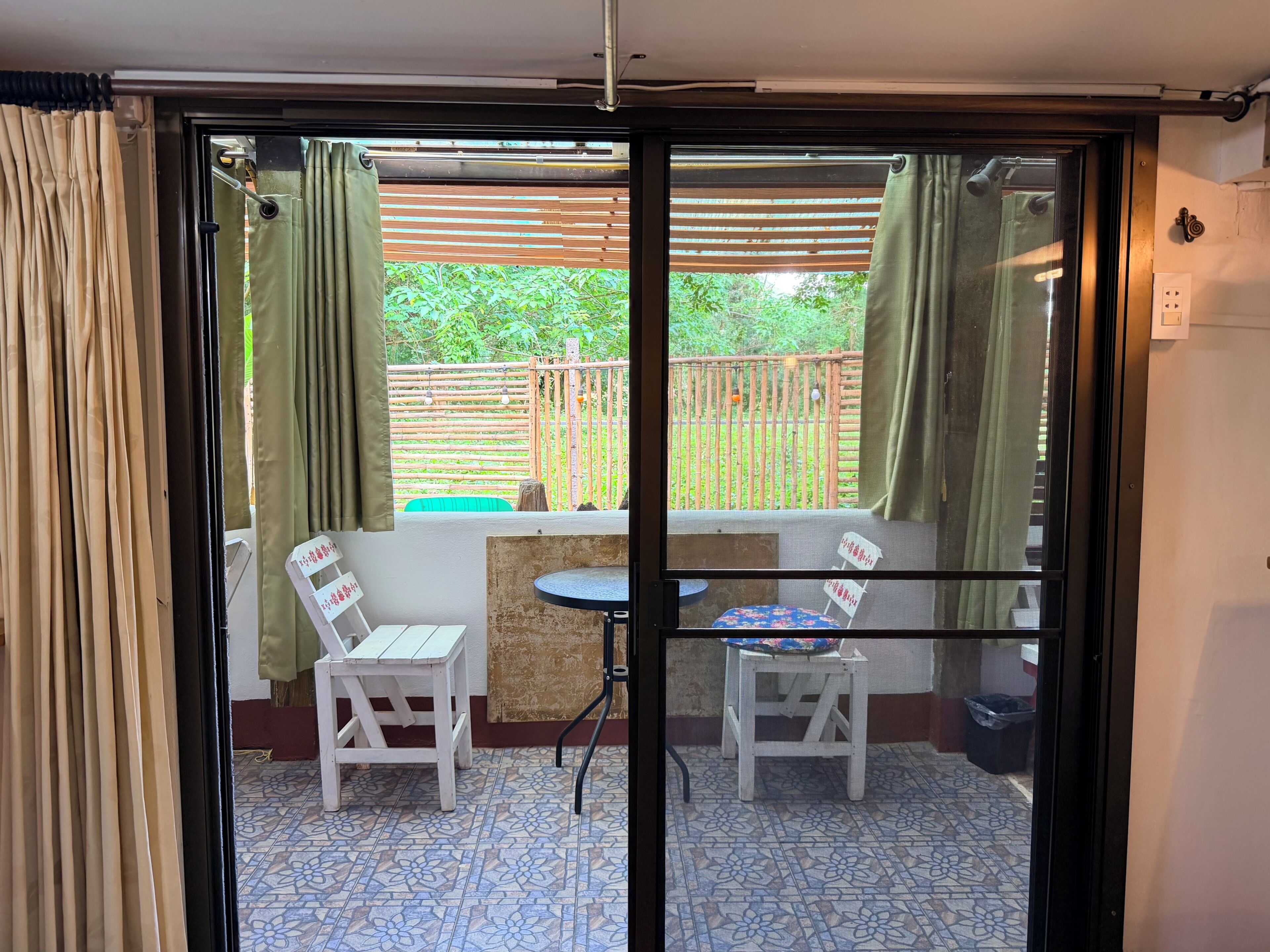 A room with a sliding glass door leading to an outdoor area with a table and chairs, a small stool, and a patterned floor.