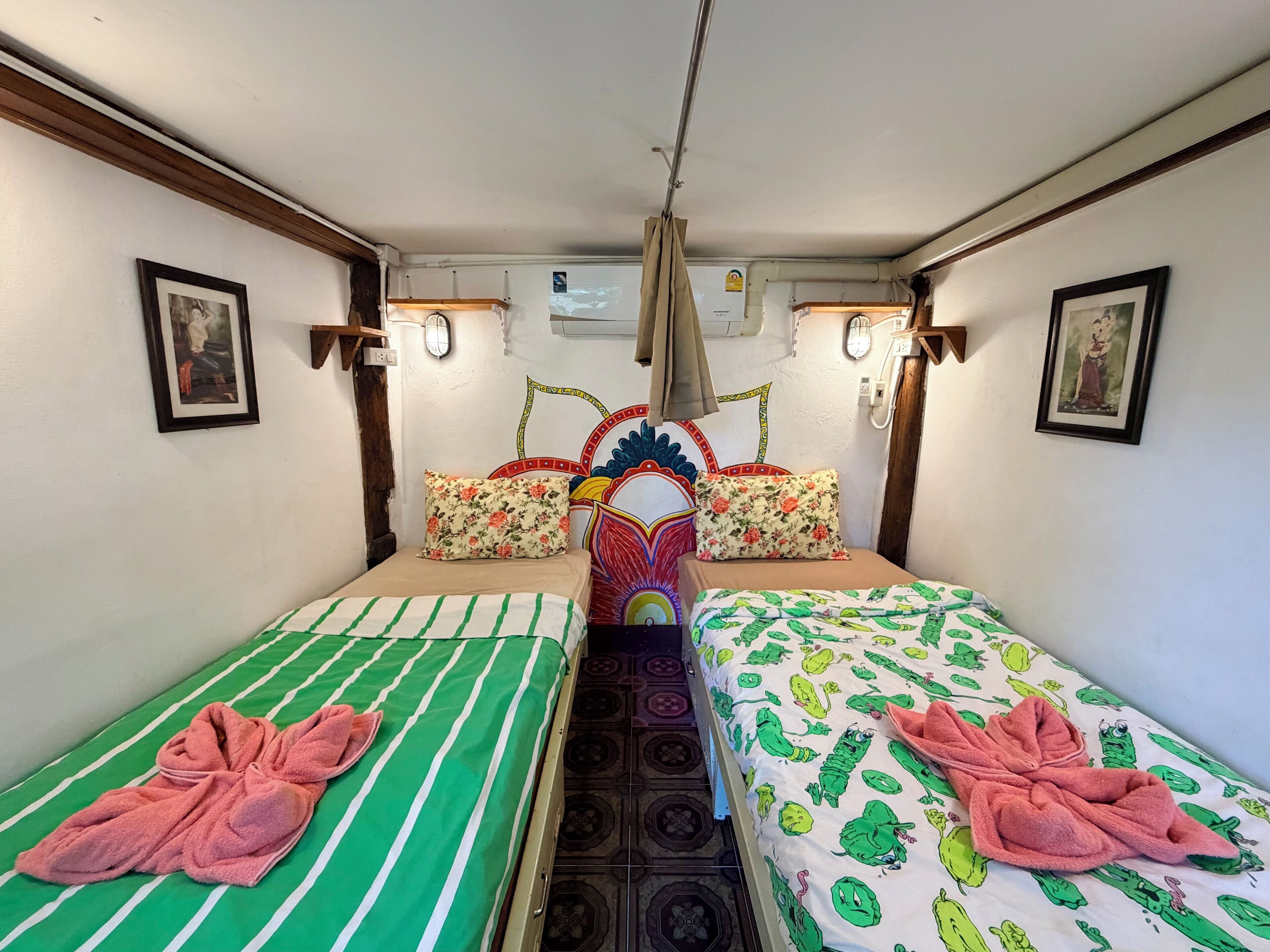 Habitación con dos camas, cada una con almohada y toalla. Cuenta con luces de pared y un ventilador de techo.