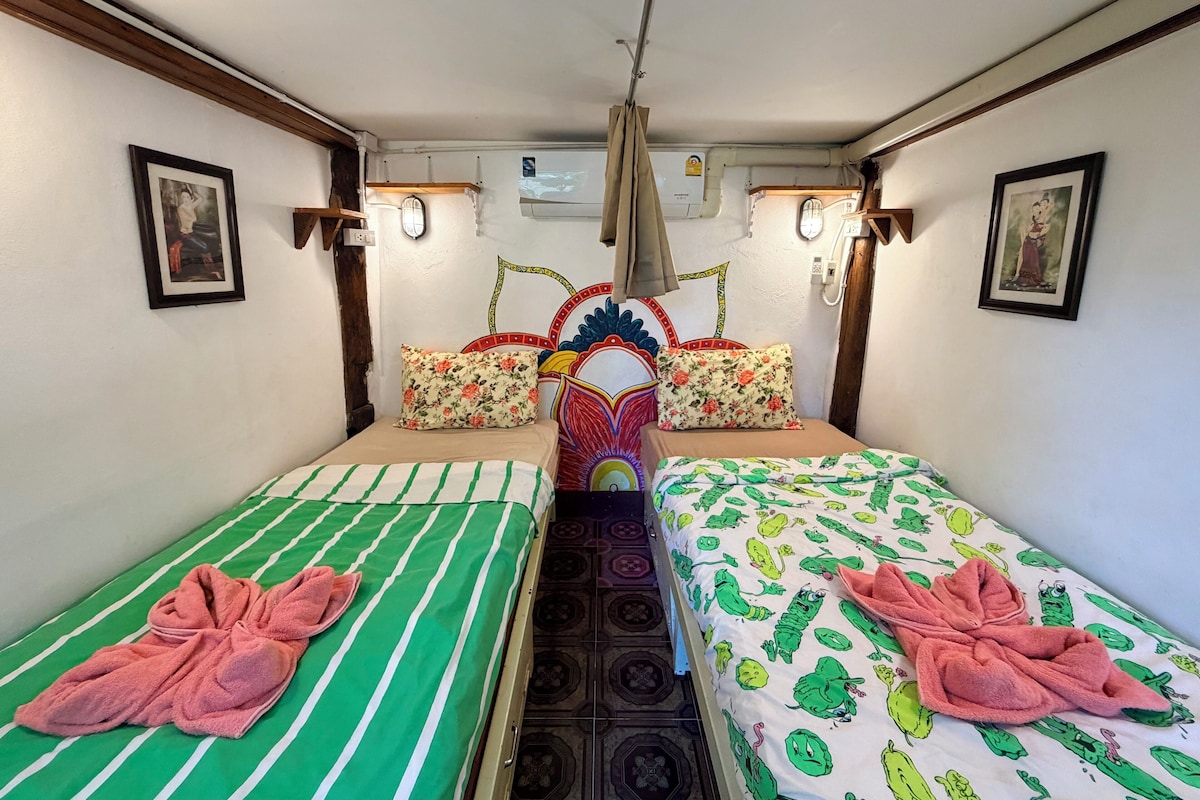 A room with two beds, each with a pillow and a towel. There are wall-mounted lights and a ceiling fan.