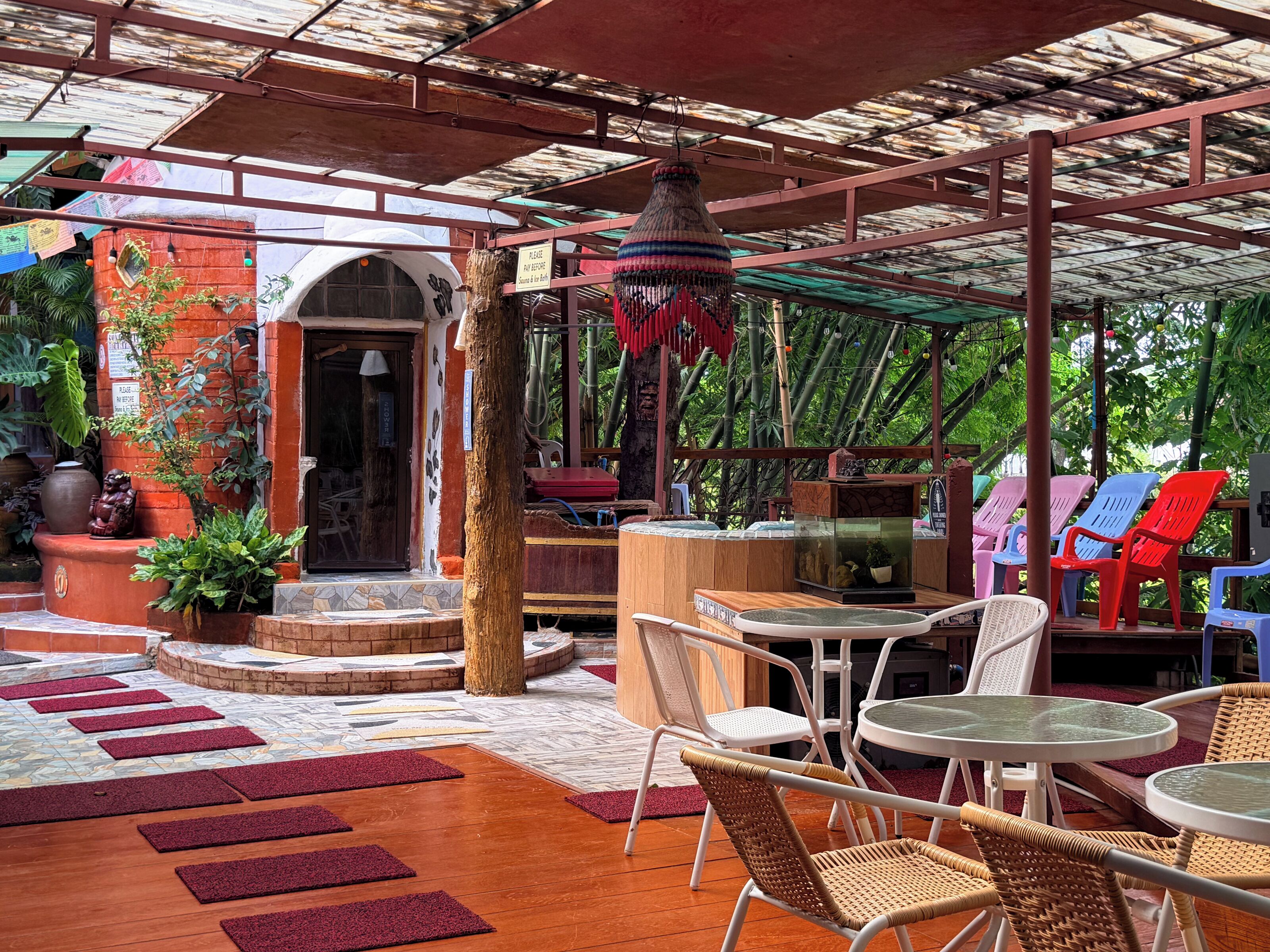 An outdoor seating area with wicker chairs and tables, a wooden bench, and a hanging lamp.