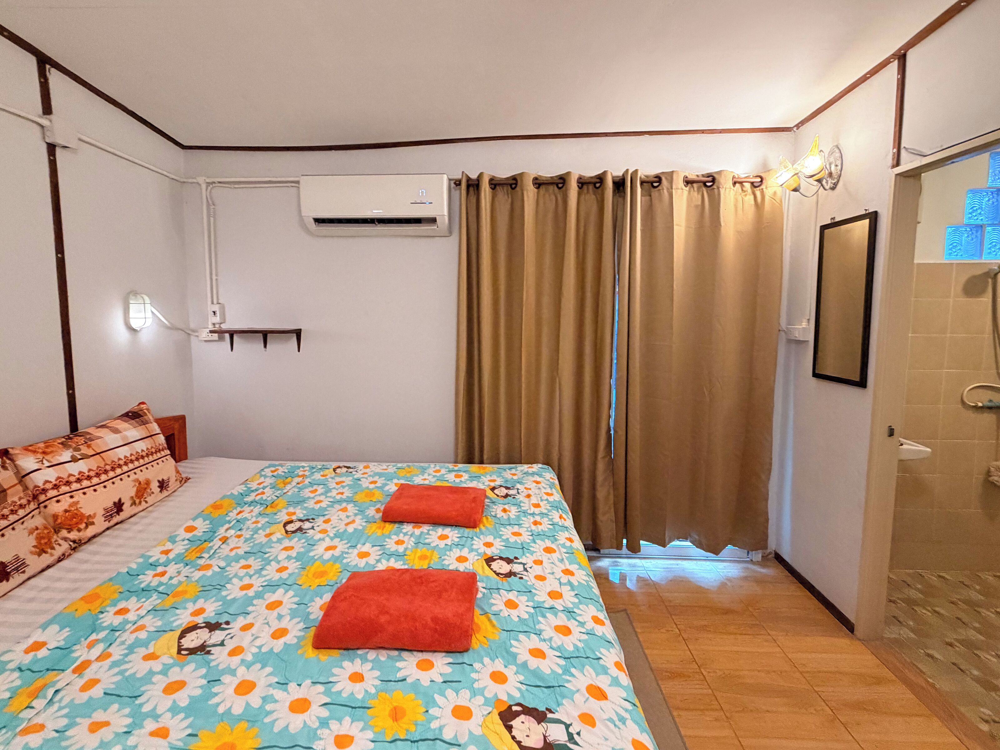 A hotel room with a bed, curtains, an air conditioning unit, a bedside lamp, and a shower area.