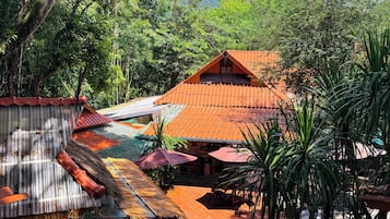 A traditional wooden structure with a thatched roof, surrounded by lush greenery and a mountain in the background.