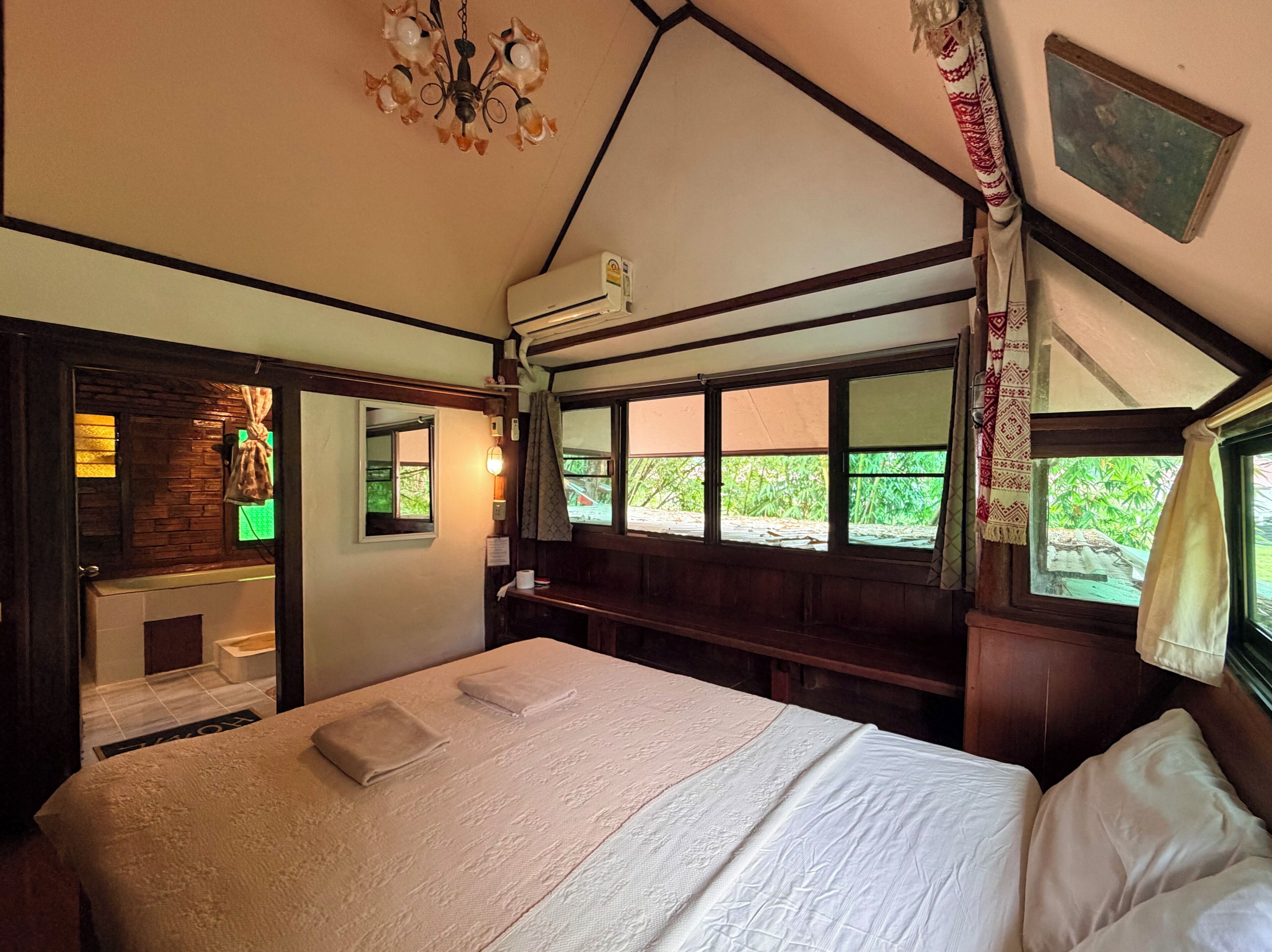 A bedroom with a bed, a chandelier, a window with a view, and a bathroom with a shower.