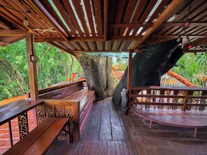 A wooden deck with benches and a railing, surrounded by lush greenery.