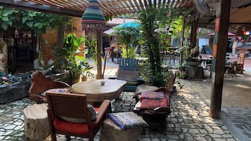 Un área de estar al aire libre con piso de piedra, mobiliario de madera y abundante vegetación.