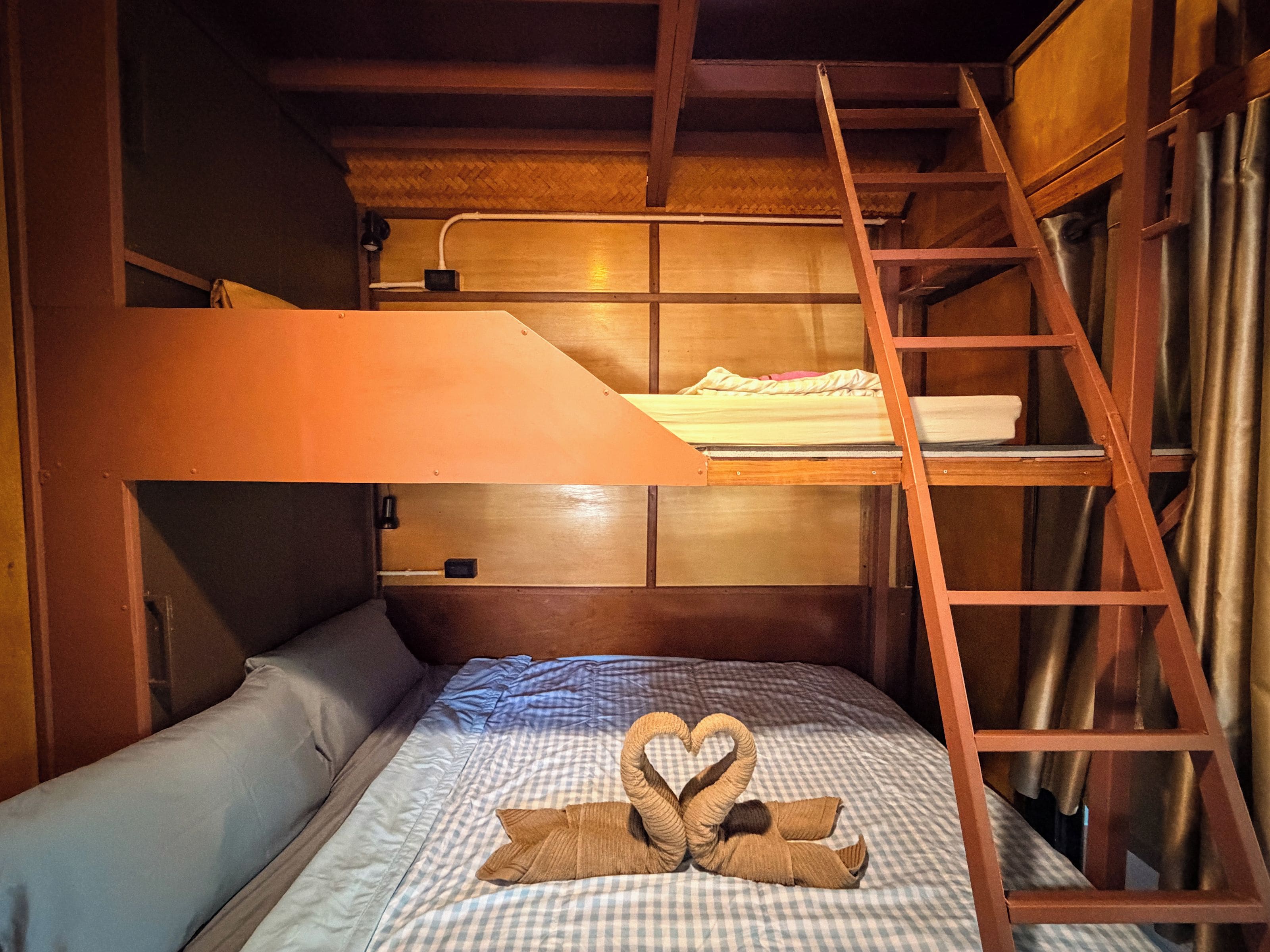 A bunk bed with a ladder, a checkered bedspread, and a heart-shaped towel arrangement.
