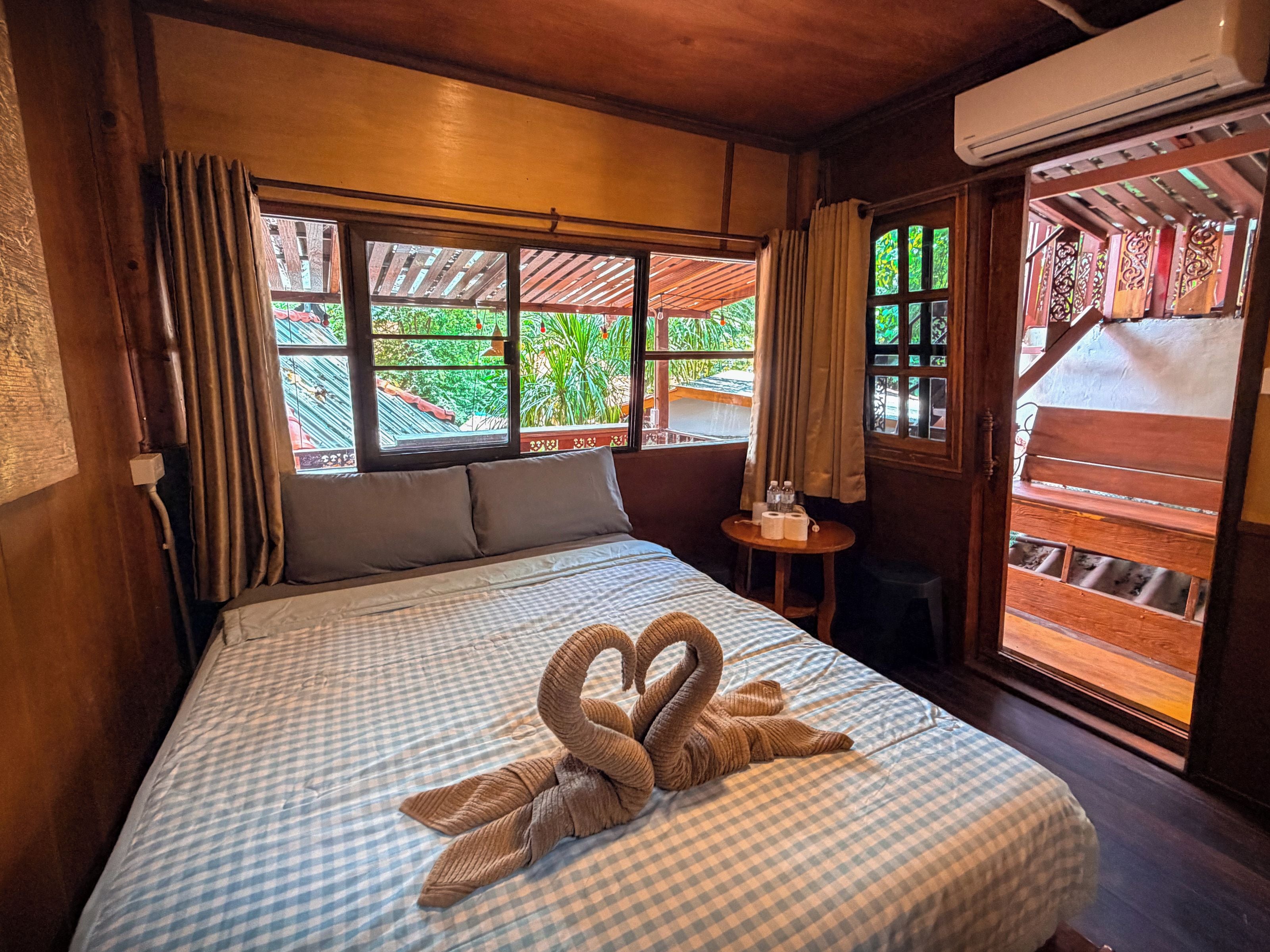 Ein Hotelzimmer mit Bett, einem kleinen Tisch mit Stuhl, einem Fenster mit Vorhängen und einer Klimaanlage.