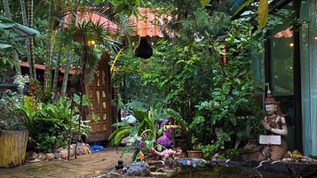 Un exuberante jardín con diversas plantas, una puerta de madera y una estatua.
