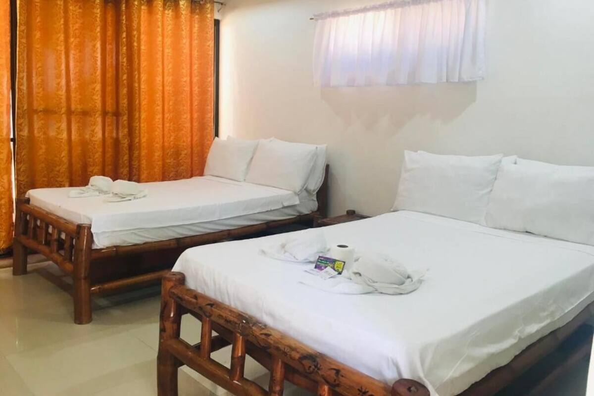 Two wooden beds with white linens, a wooden headboard, and a window with a sheer curtain.
