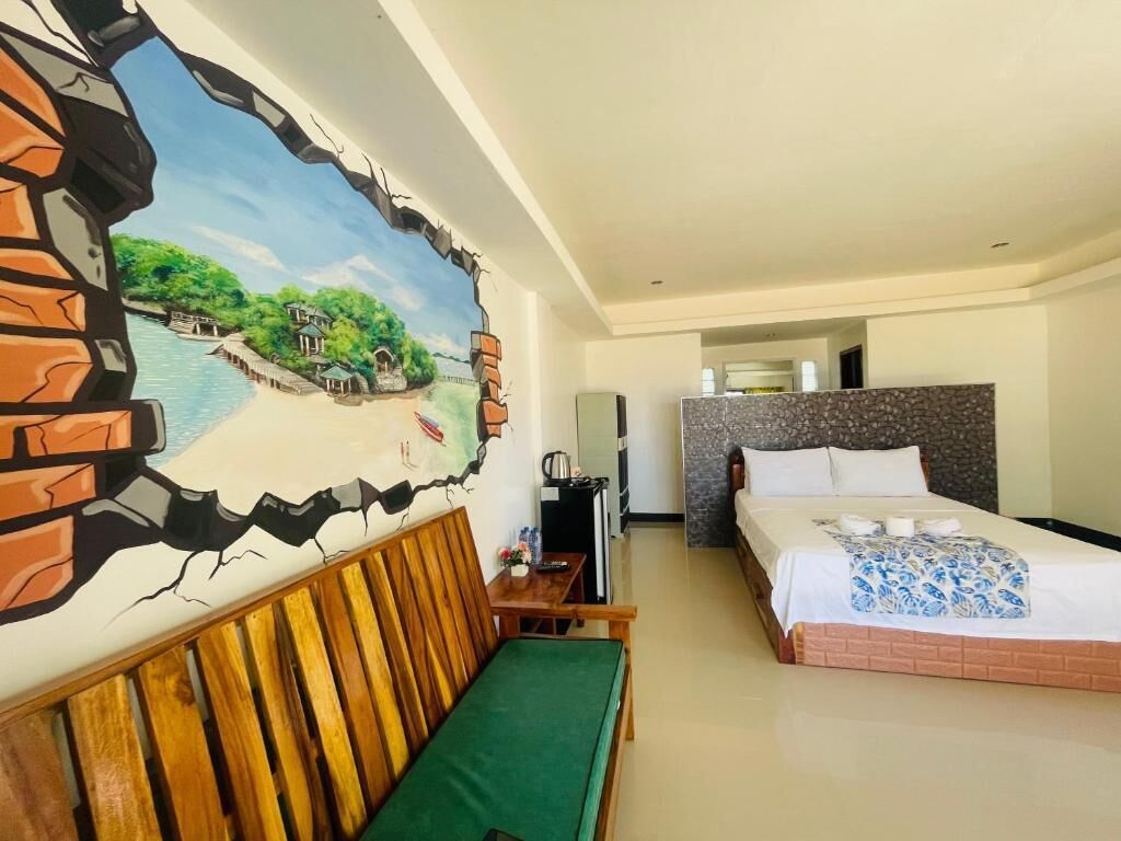 A hotel room with a bed, a green sofa, a TV, and a painting of a landscape.
