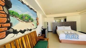 A hotel room with a bed, a green sofa, a TV, and a painting of a landscape.