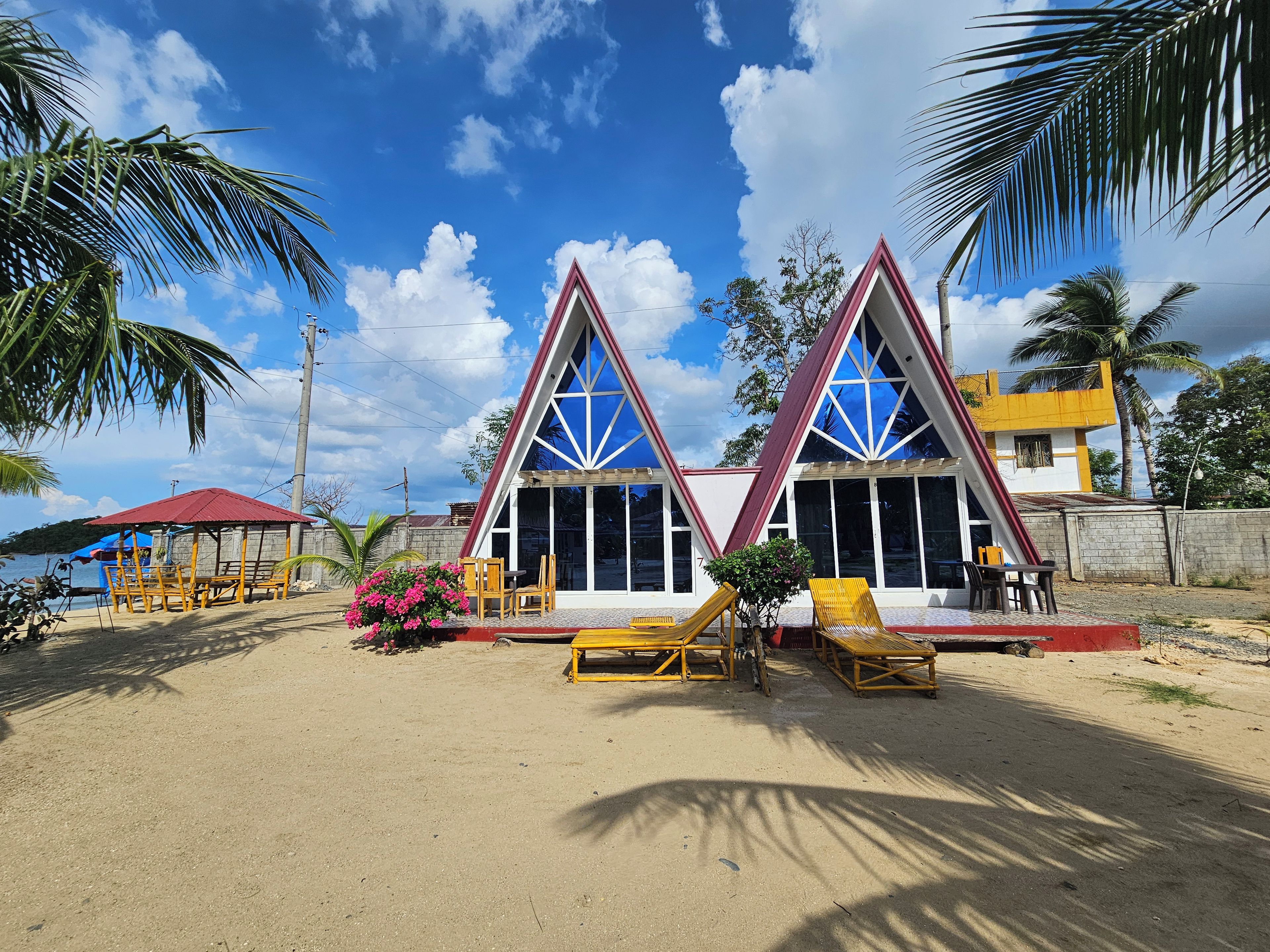 A beachside building with a triangular roof, outdoor seating, and a view of the sea.