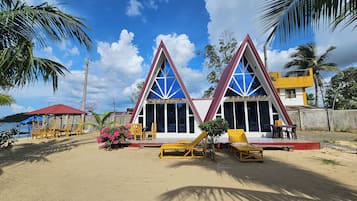 A beachside building with a triangular roof, outdoor seating, and a view of the sea.