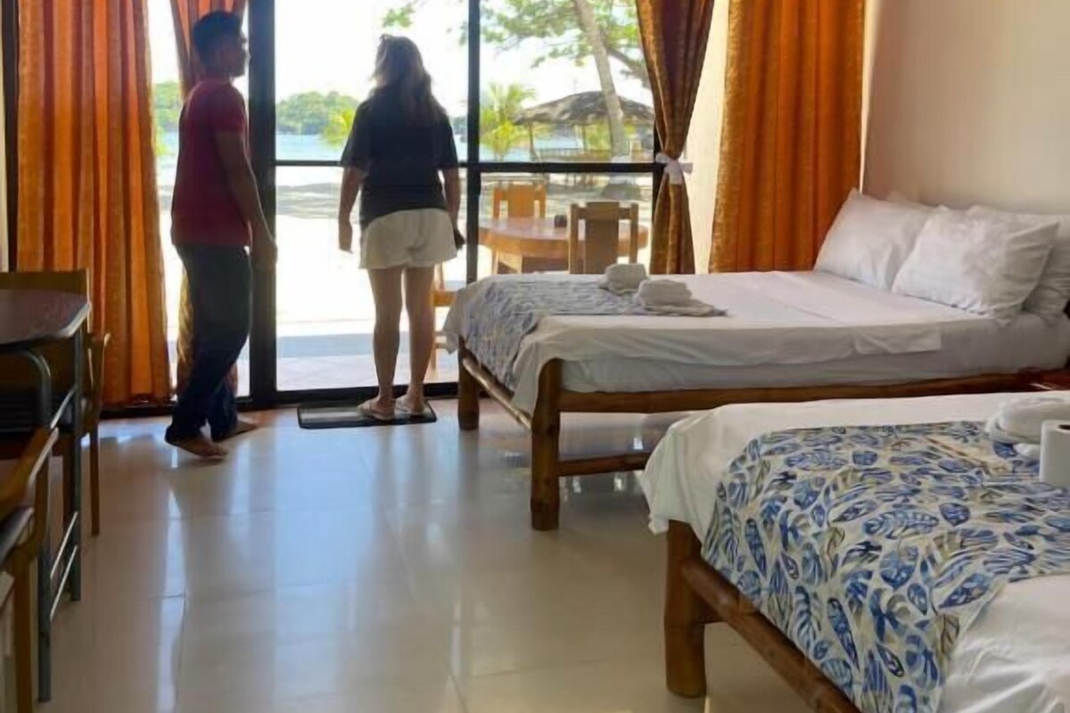 A hotel room with two beds, a dining area, and a large window with curtains.