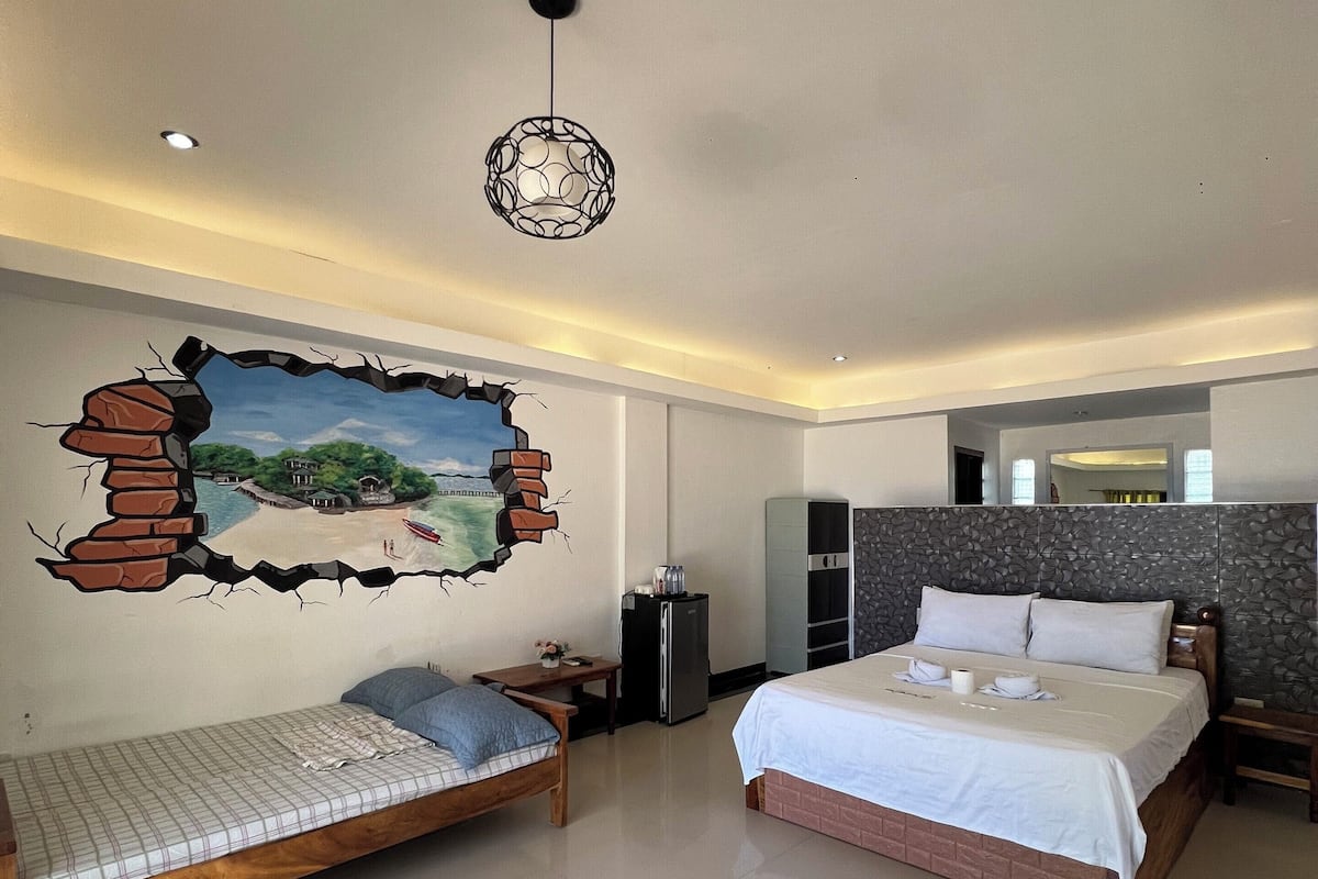 A bedroom with two beds, a refrigerator, a wall with a cracked surface design, and a hanging light fixture.