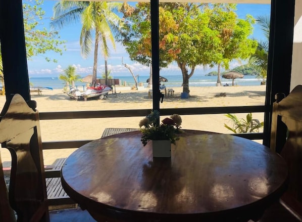 Una mesa de madera redonda con un centro de flores, con vista a una playa con palmeras y un bote.