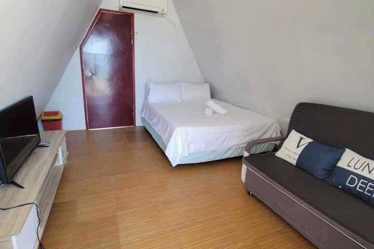 A small, compact room with a bed, a sofa, a TV, and a ceiling fan.