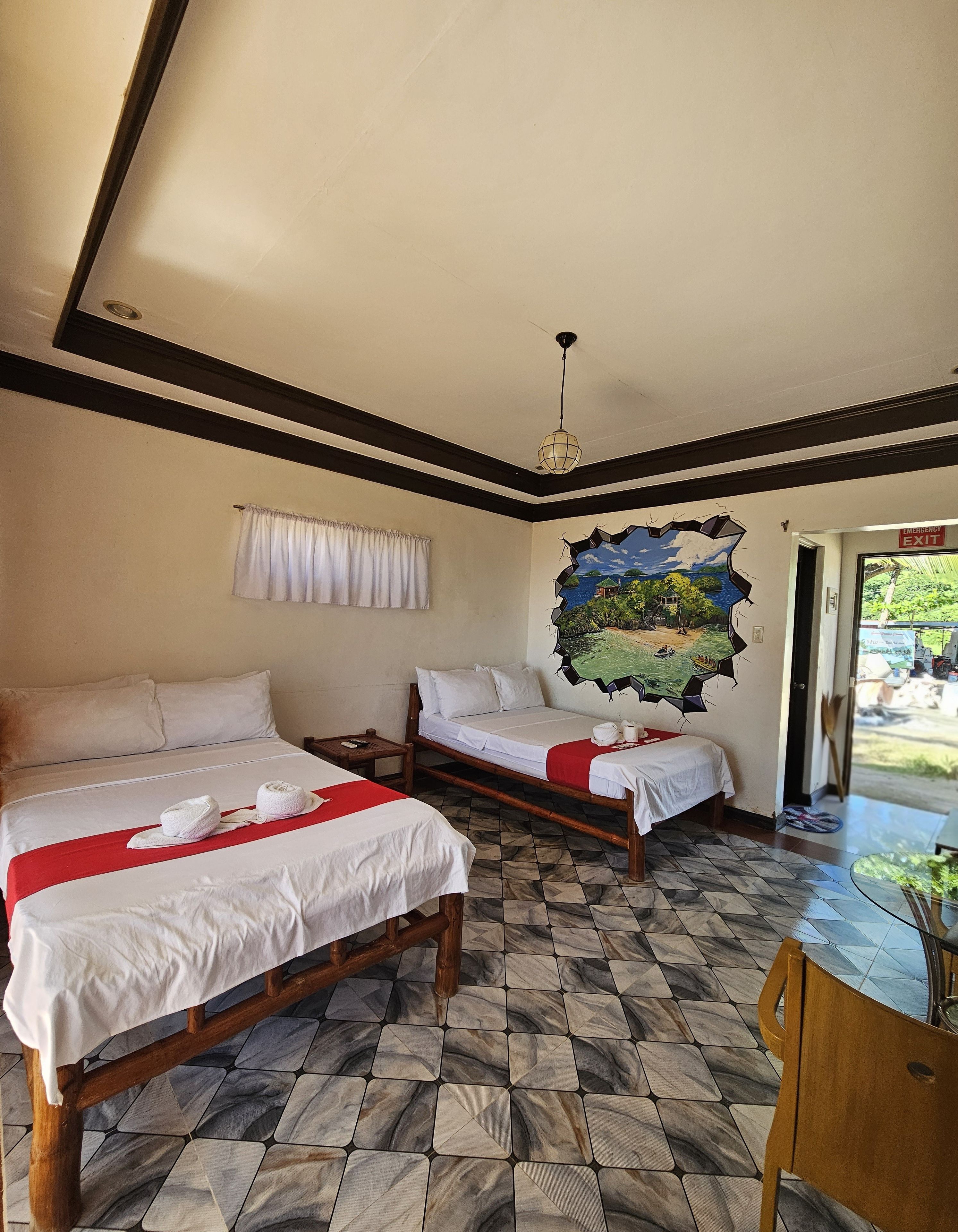 A hotel room with two beds, a mural, a dining area, and a view of the outdoors.