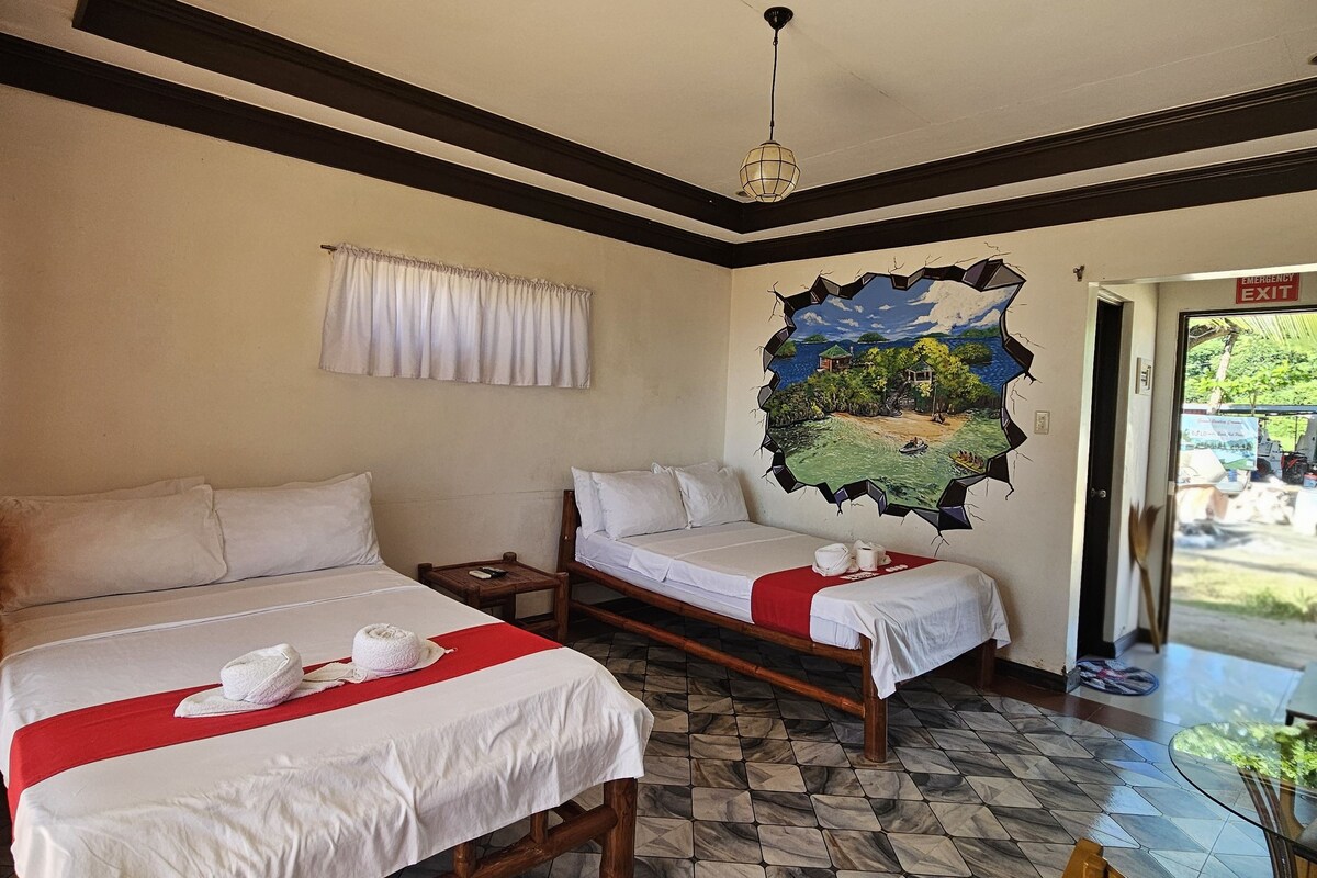 A hotel room with two beds, a mural, a dining area, and a view of the outdoors.