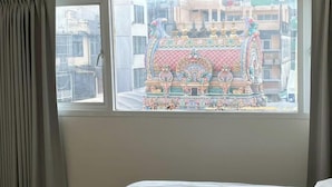 A bedroom with a bed, a window, and a view of a colorful building outside. - Prime Silom (Bangkok)