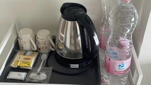 A minibar with a coffee maker, two mugs, Lipton tea, a spoon, and a bottle of water. - Prime Silom (Bangkok)