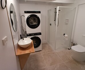 A compact bathroom with a washing machine, a sink, a toilet, and a glass-enclosed shower. - Beautiful Byron hinterland retreat. 20 mins to Byron Bay, Bangalow and Ballina. (Clunes)