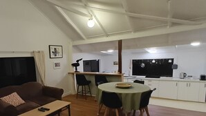 Una sala de estar con un sofá, una mesa de centro y un comedor con una mesa y sillas. Hay una cocina con armarios y una ventana.