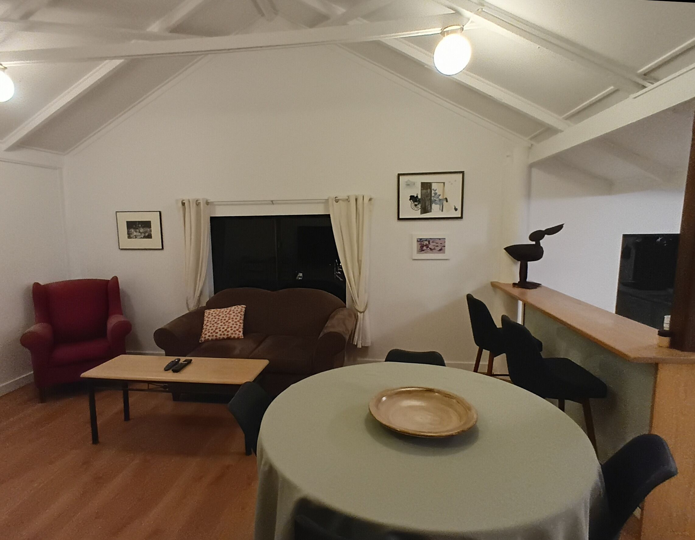 Uma sala de estar acolhedora com um sofá marrom, uma poltrona vermelha, uma mesa pequena e um espaço de jantar com uma mesa redonda e cadeiras.