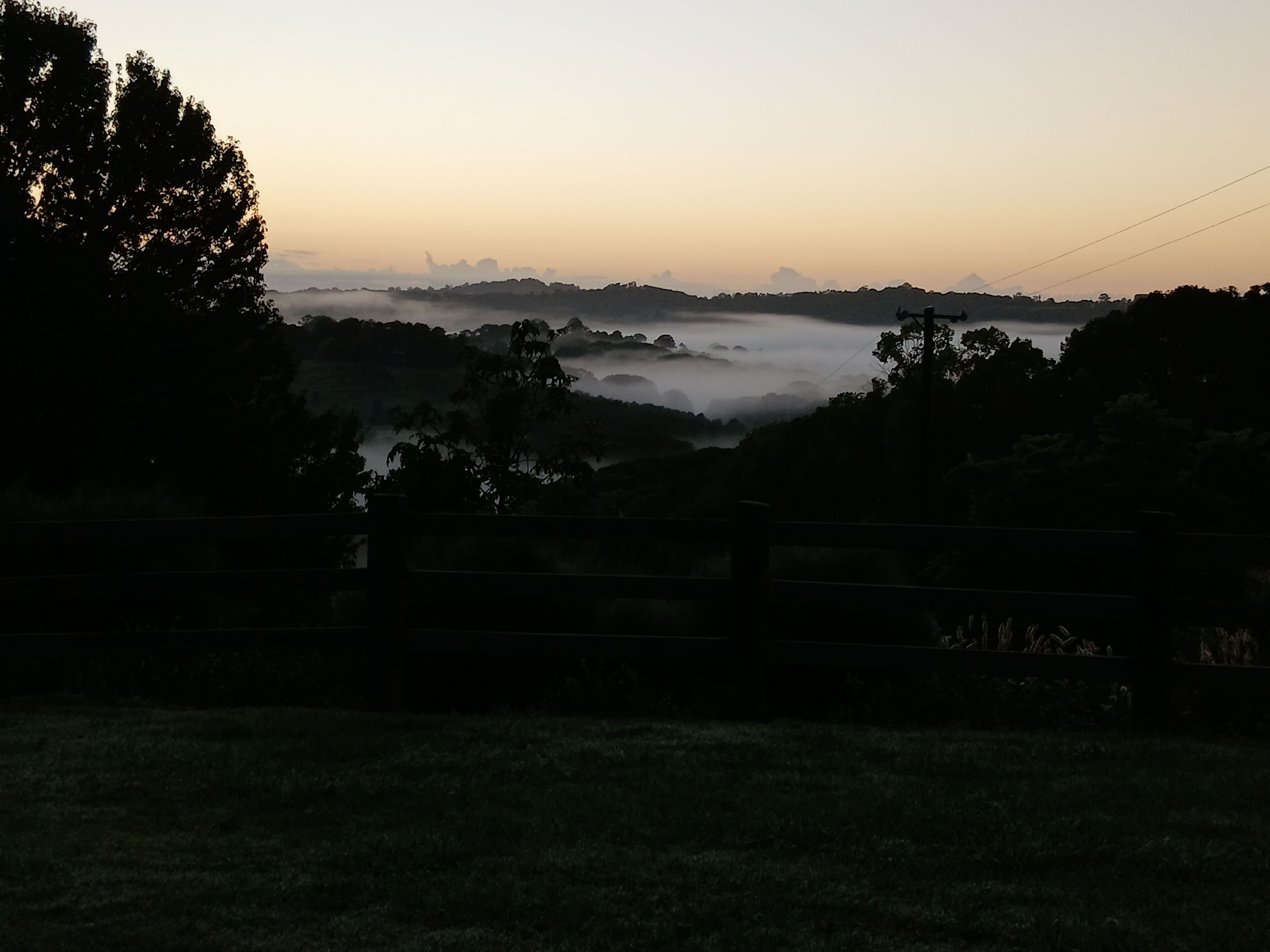 A rural landscape with a fence in the foreground, a misty valley, and a distant mountain range.