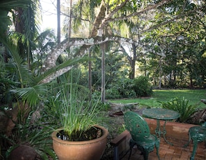 A garden with a patio area, including a table and chairs, surrounded by lush greenery and trees.