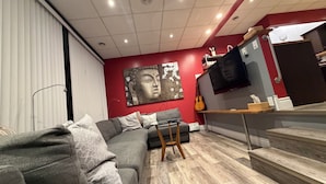 Un soggiorno moderno con un divano grigio, un tavolino in legno, una TV a parete e una scala che conduce a un altro livello.
