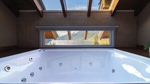 A hot tub with a view of mountains through a skylight.