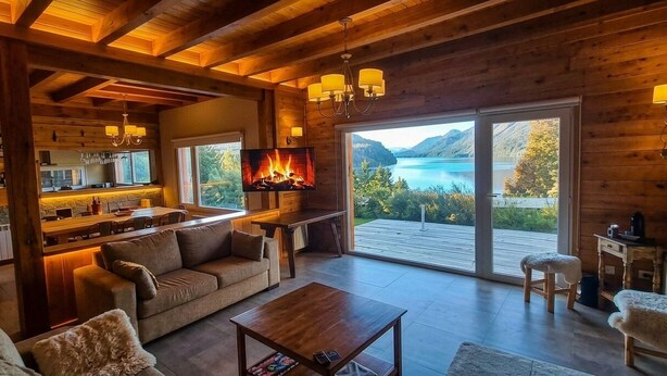 A cozy cabin with a fireplace, a dining area, and a large window overlooking a lake.