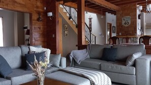 A cozy living room with a grey sofa, a coffee table with a vase, and a staircase with a wall clock.