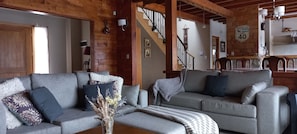 Un salon chaleureux avec un canapé gris, une table basse ornée d’un vase et un escalier avec une horloge murale.