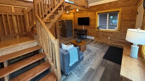 A wooden interior with a staircase, a flat-screen TV, a dining area, and a window.
